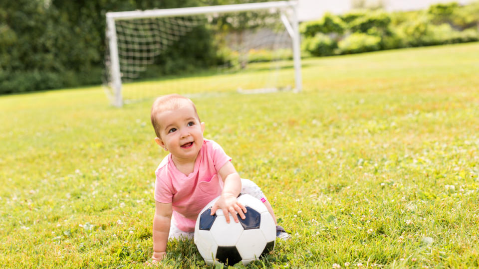 baby girl playing on grass with football - stock photo