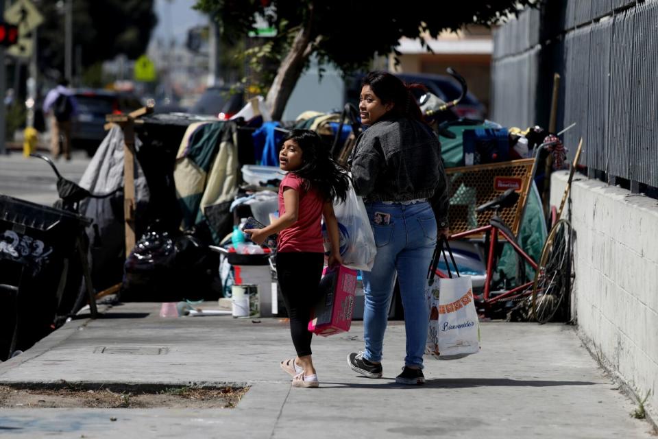 A young girl and a woman look before walking into the street to get around a homeless encampment