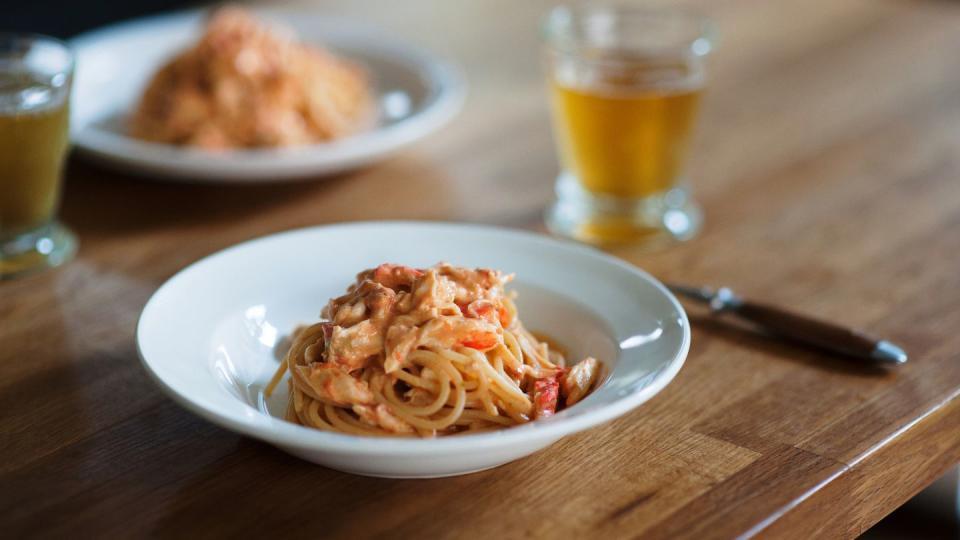 a snapshot of spaghetti lunch tomato cream pasta with king crab on a white plate, a glass of beer, and a wooden handle folk