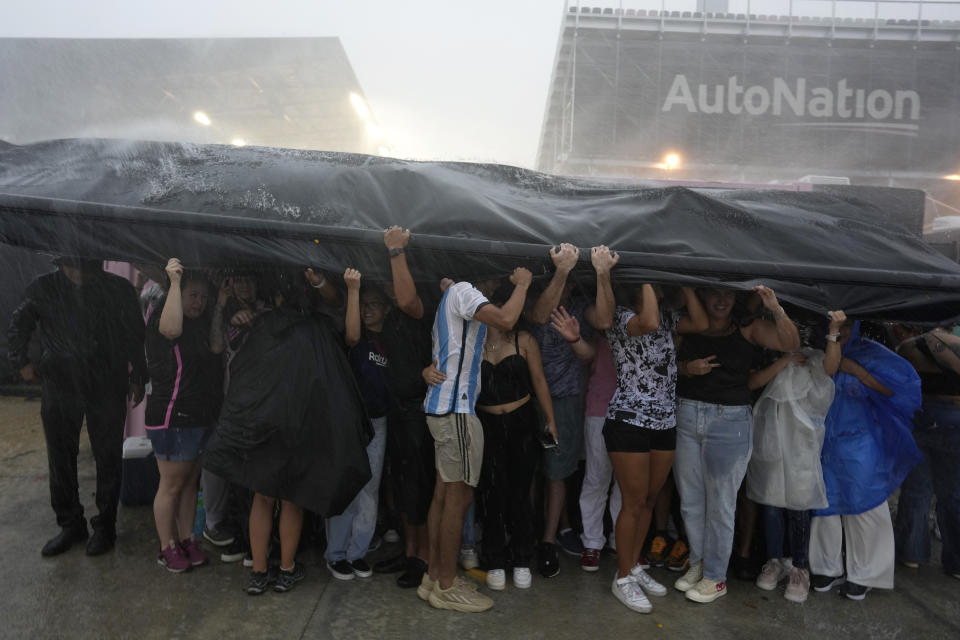 Fans seek shelter from a torrential downpour as they wait to enter DRV PNK Stadium, home of the Inter Miami MLS soccer team, for an event to present international superstar Lionel Messi one day after the team finalized his signing through the 2025 season, Sunday, July 16, 2023, in Fort Lauderdale, Fla. (AP Photo/Rebecca Blackwell)