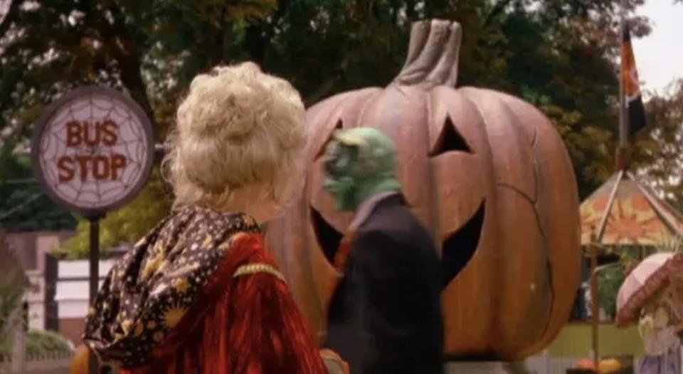 woman with blonde hair looking at a big pumpkin