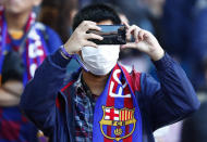 A Barcelona fan wears a face mask in an attempt to protect there self from the coronavirus uses his mobile prior a Spanish La Liga soccer match between Barcelona and Real Sociedad at the Camp Nou stadium in Barcelona, Spain, Saturday, March 7, 2020. (AP Photo/Joan Monfort)