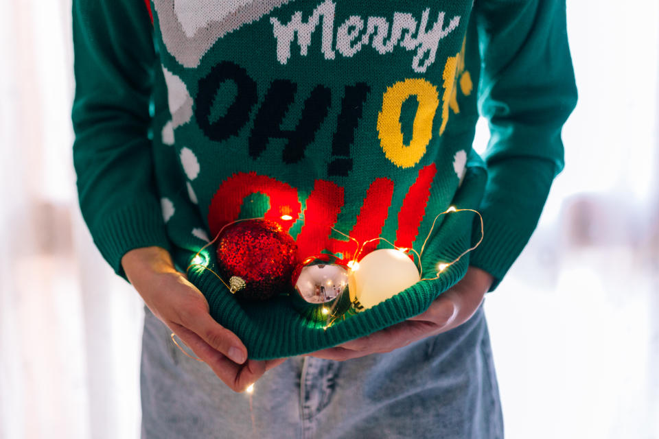 Unrecognizable woman holding Christmas tree balls in a Christmas jumper with lights