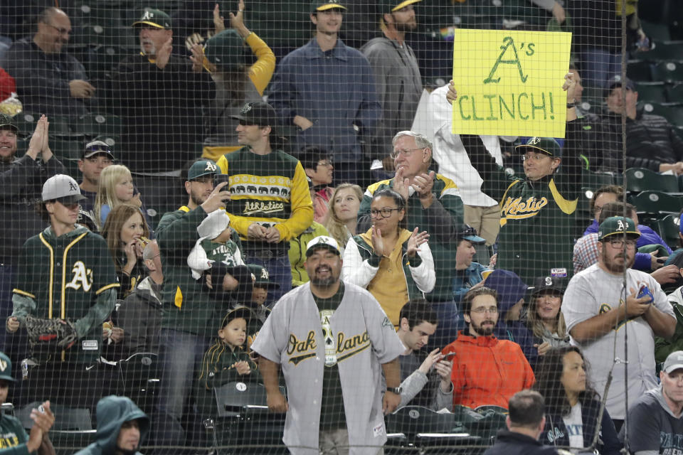 A fan holds a sign that reads "A's Clinch!" during the first inning of a baseball game against the Seattle Mariners, Friday, Sept. 27, 2019, in Seattle. The Athletics clinched a wild-card berth in the American League before the first pitch of their game when the Cleveland Indians lost to the Washington Nationals. (AP Photo/Ted S. Warren)