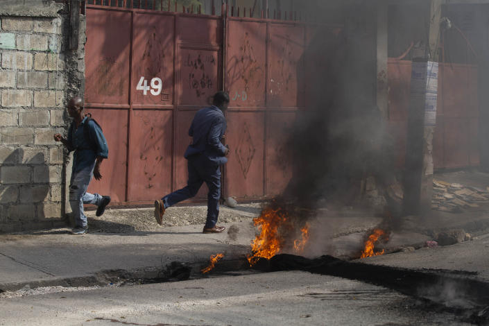 Pedestrians walk past a burning barricade set up by friends and relatives of James Philistin who was kidnapped last night, in Port-au-Prince, Haiti, Wednesday, Nov. 24, 2021. (AP Photo/Odelyn Joseph)
