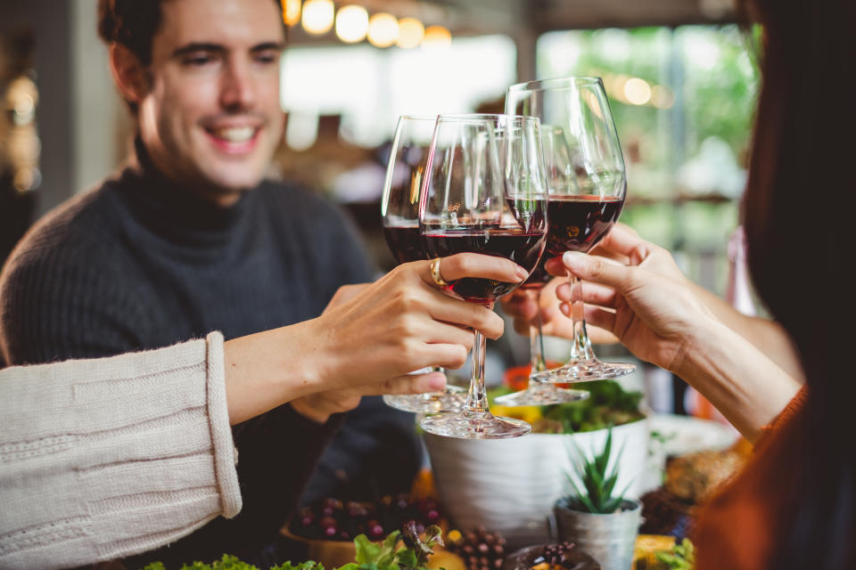 Group of young people celebrating Christmas party dinner with clinking glass of wine