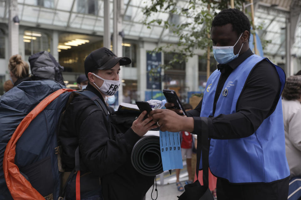 A railway employee, right, checks the COVID-19 health pass that everyone in the country needs to enter cafes, trains and other venues, Monday Aug.9, 2021 at the Gare de Lyon train station in Paris. Starting today, the pass will be required in France to access cafes, restaurants, long-distance travel and, in some cases, hospitals. It was already in place for cultural and recreational venues, including cinemas, concert halls, sports arenas and theme parks with a capacity for more than 50 people. (AP Photo/Adrienne Surprenant)