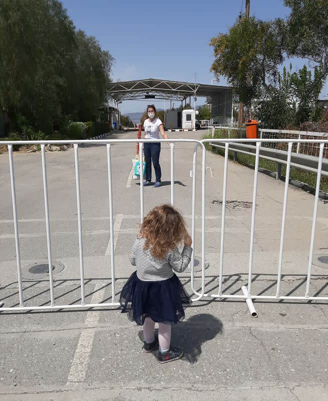 Olivia Shule stands behind a metal barrier as she greets her grandmother at the UN controlled buffer zone at the Ayios Dhometios crossing, known as Metehan in Turkish, following the coronavirus disease (COVID-19) outbreak, in Nicosia