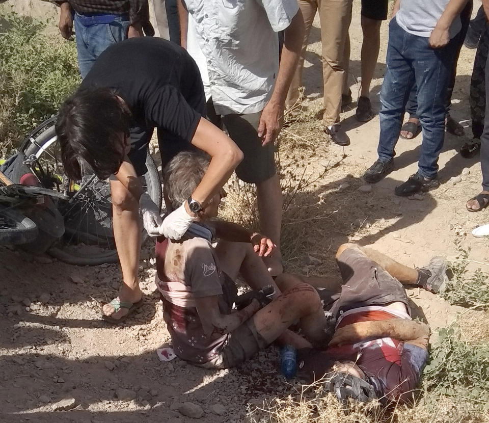 In this photo taken on Sunday, July 29, 2018, a woman helps a wounded cyclist, where the four tourists were killed when a car rammed into a group of foreigners on bicycles south of the capital of Dushanbe, Tajikistan. The Islamic State group on Tuesday claimed responsibility for a car-and-knife attack on Western tourists cycling in Tajikistan that killed two Americans and two Europeans. (AP Photo/Zuly Rahmatova)