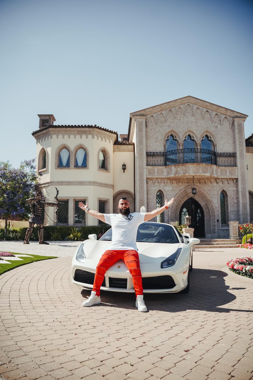 A man sitting on a white sports car in front of a mansion.