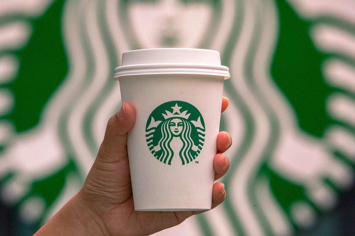 A Starbucks coffee cup against a Starbucks logo