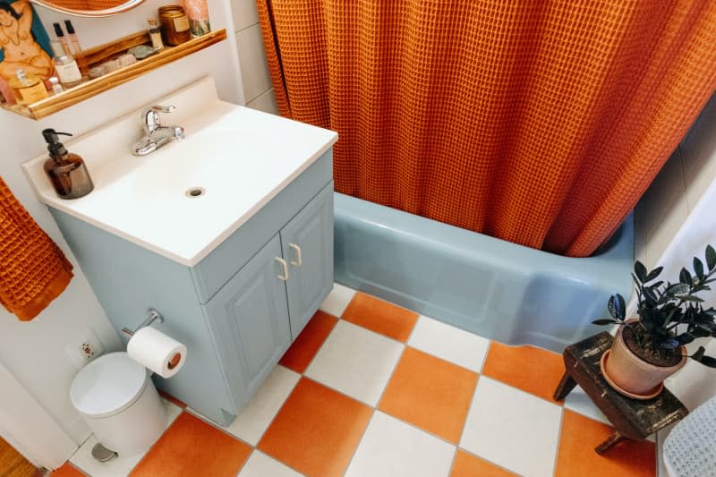 Blue sink cabinet and tub are seen in white bathroom with orange checkerboard floor.