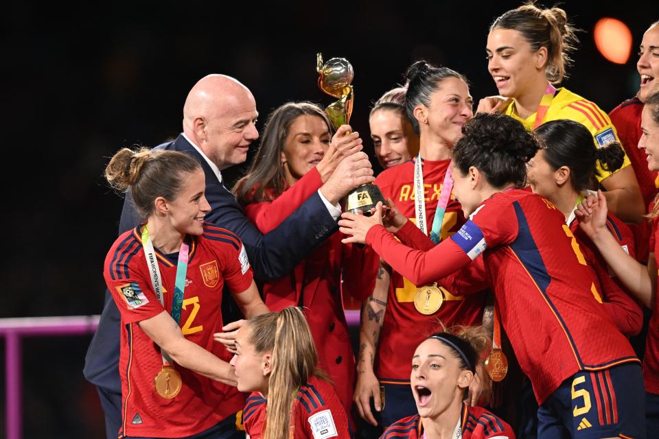 FIFA President Gianni Infantino (2L) and Queen Letizia of Spain (3L) hold the trophy with Spain's defender #05 Ivana Andres as Spain's players celebrate on the podium after winning the Australia and New Zealand 2023 Women's World Cup final football match between Spain and England at Stadium Australia in Sydney on August 20, 2023. (Photo by Izhar KHAN / AFP) (Photo by IZHAR KHAN/AFP via Getty Images)