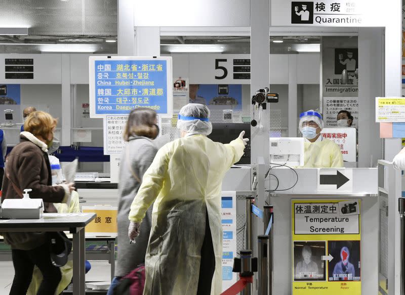 Officials in protective suits check passengers arriving from South Korea at a quarantine station at Narita international airport in Narita