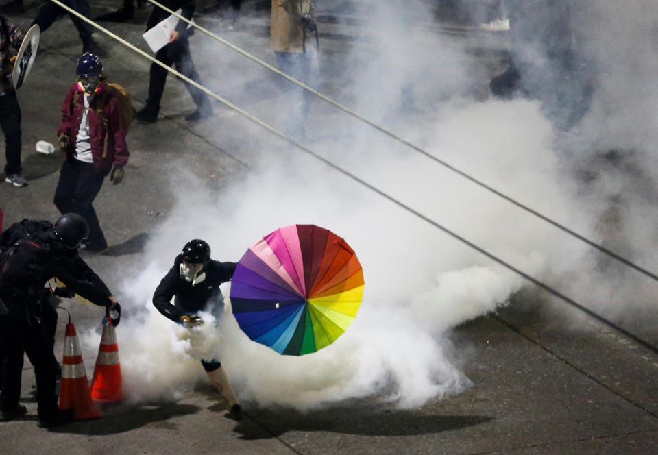 A protester with a rainbow umbrella picks up a gas canister as law enforcement deploys chemical agents and blast balls during a protest against racial inequality in the aftermath of the death in Minneapolis police custody of George Floyd, near the Seattle Police department's East Precinct in Seattle, Washington.
