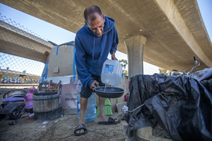 Los Angeles, CA - July 06: Jose Luis Camargo, 55, washes out a skillet outside his makeshift tent, under an elevated ramp linking the 110 to the 105 on Wednesday, July 6, 2022, in Los Angeles, CA. He is preparing to heat up water for his ramen. (Francine Orr / Los Angeles Times)