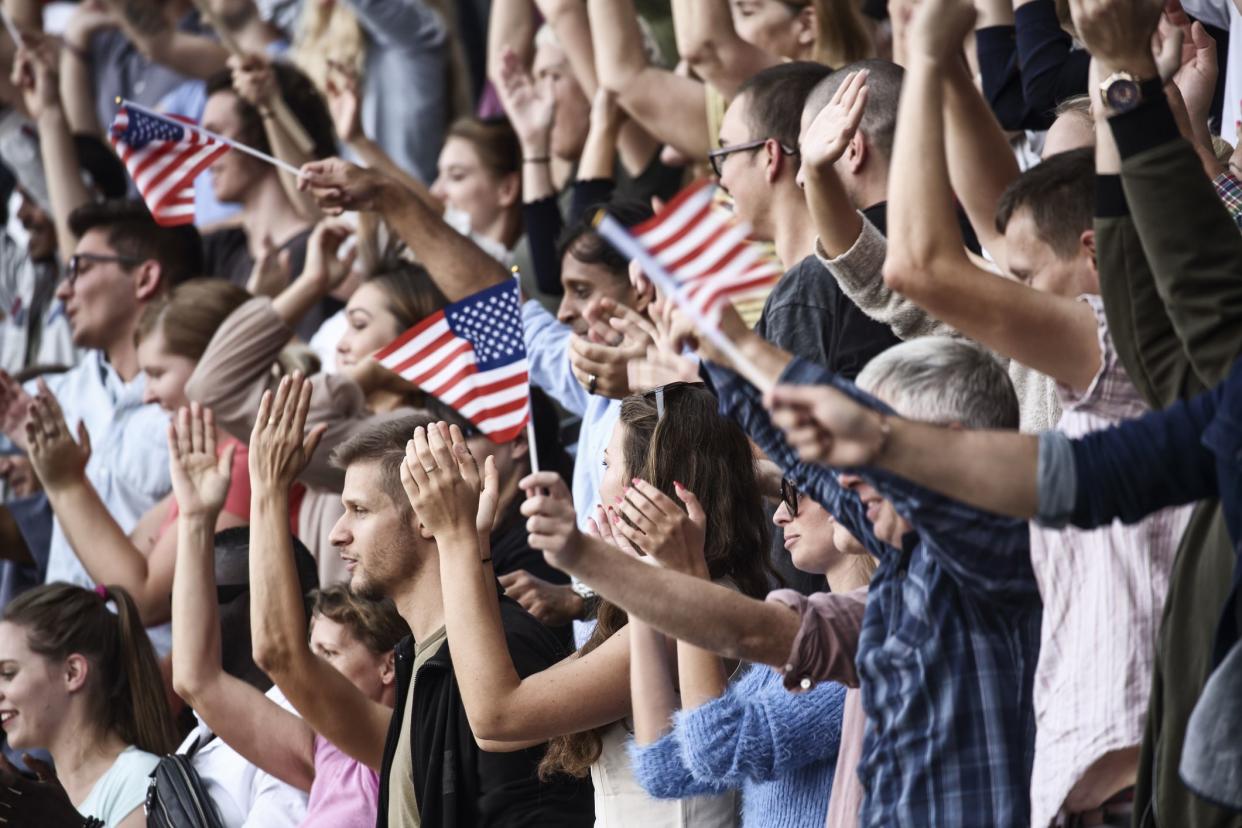 USA colored flags waving above large crowd on a stadium.