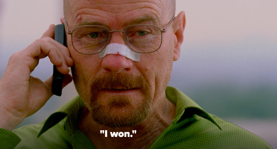 Walter White with a bandaged nose, wearing glasses and a green shirt, is talking on a cellphone