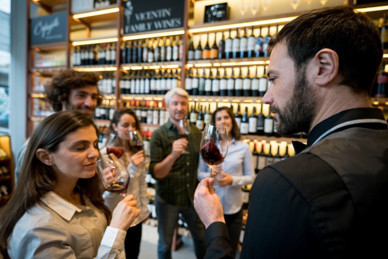 Group of people at a wine tasting in a winery and friendly sommelier teaching them while one woman is smelling the wine with eyes closed