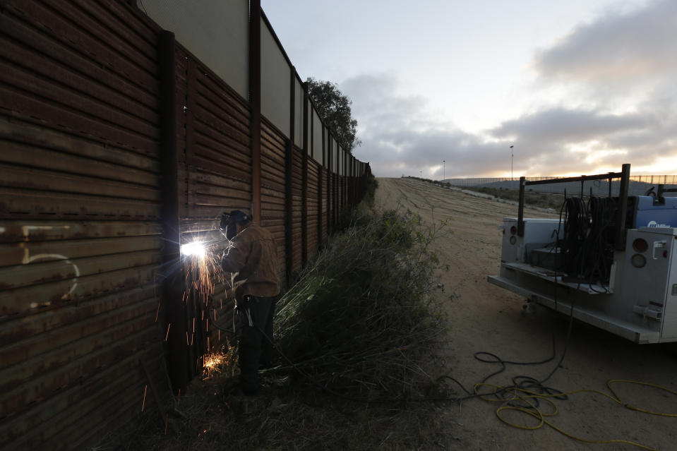 ARCHIVO - En esta imagen de archivo del 13 de junio de 2013, un agente de la patrulla fronteriza de Estados Unidos trabaja con un equipo de reparación para soldar un agujero en un tramo de muro fronterizo de acero, en San Diego. (AP Foto/Gregory Bull, Archivo)