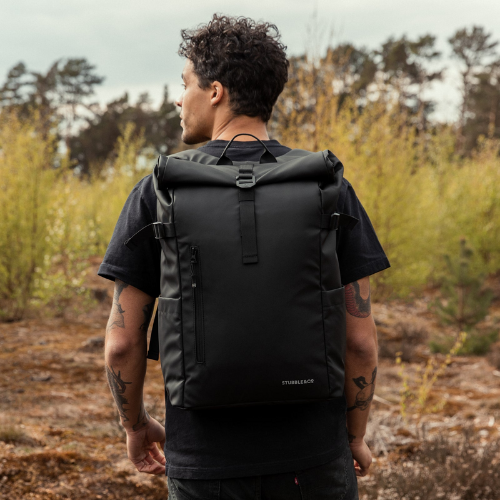man wearing Stubble & Co. Roll Top Backpack walking through forestry