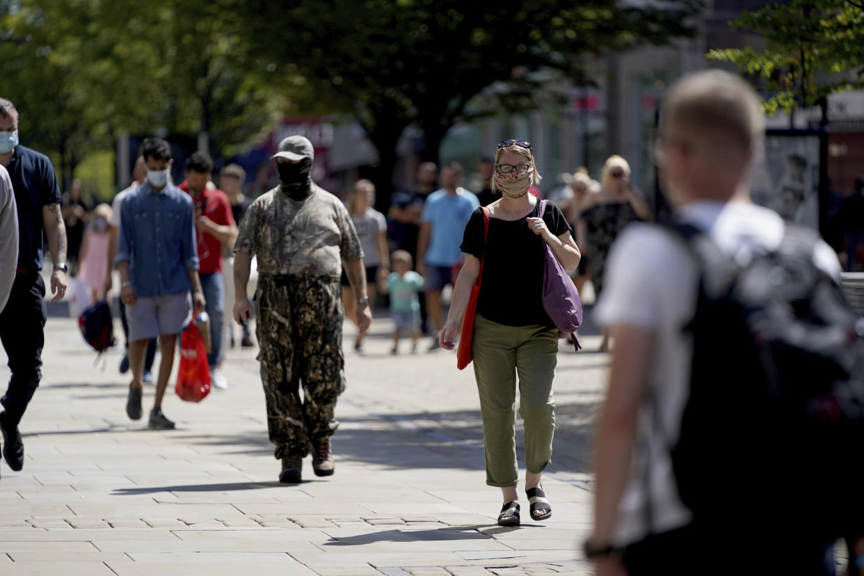 People walk wearing face masks to try to stop the spread of coronavirus in a shopping area in Manchester, northern England, Friday, July 31, 2020. The British government on Thursday night announced new rules on gatherings in some parts of Northern England, including Manchester, that people there should not mix with other households in private homes or gardens in response to an increase trend in the number of cases of coronavirus cases per 100,000 people. (AP Photo/Jon Super)