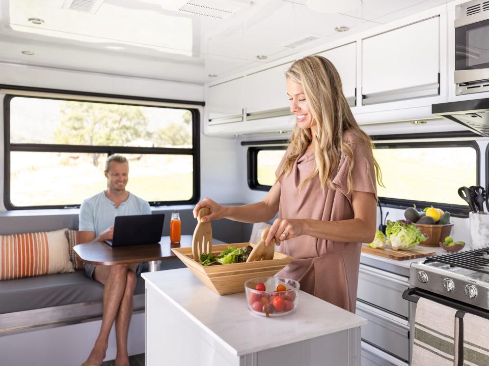 A person in the kitchen as another person types on their laptop.