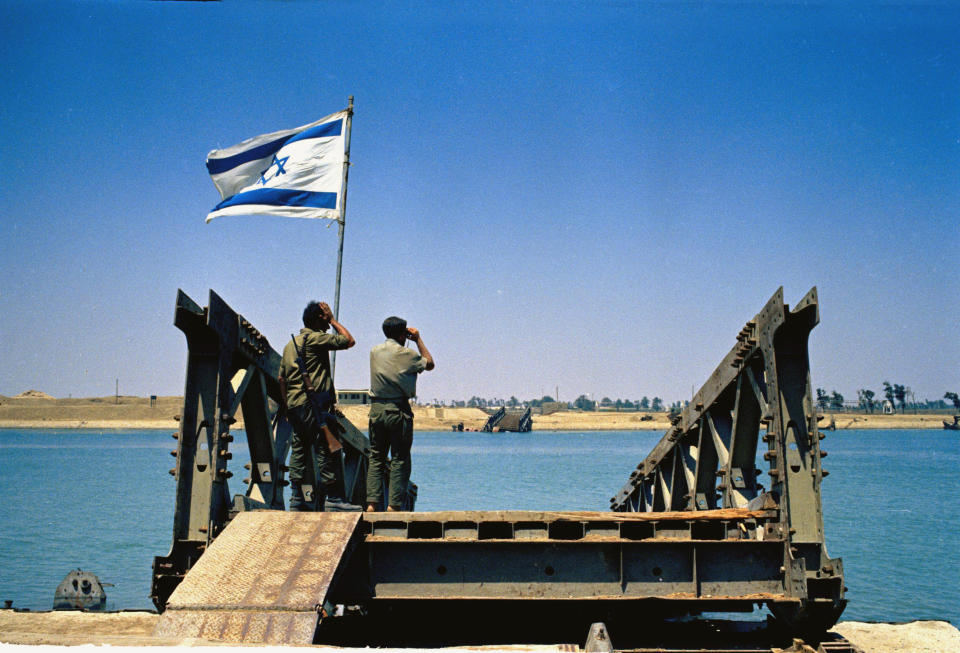 FILE - In this June 1967 file photo, Israeli soldiers stand at a destroyed bridge looking over the Egyptian bank of the Suez Canal. Since it opened in 1869, the canal has been a source of national pride and a focus of international conflict. Now, a skyscraper-sized container ship called the Ever Given got stuck sideways across the waterway since Tuesday, March 23, 2021 . The obstruction has halted canal traffic, valued at over $9 billion a day. (AP Photo/Mario Torrisi, File)