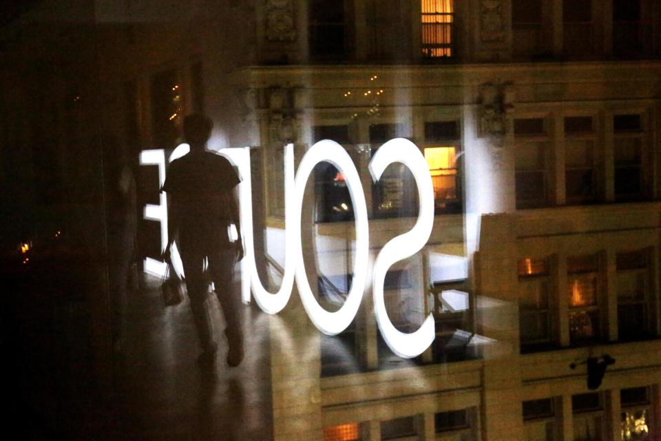 The silhouette of a person in a dark room against the reflection of the word Source in large, white letters