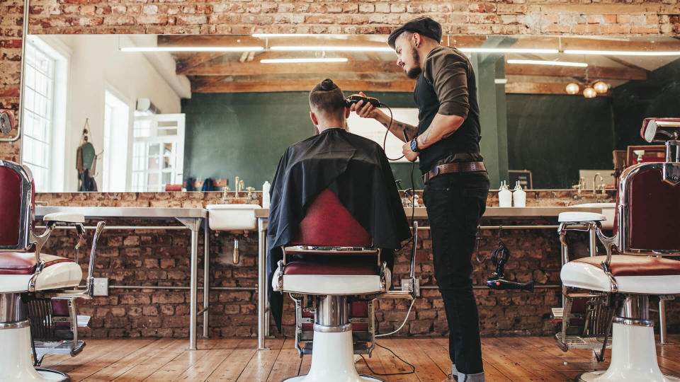 Rear view shot of handsome hairdresser cutting hair of male client.