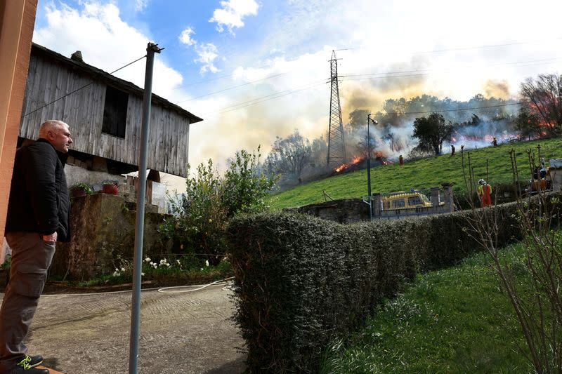 A homeowner observes firefighters tackling a blaze near the village of Setienes during an outbreak of wildfires in northern Spain's Asturias region