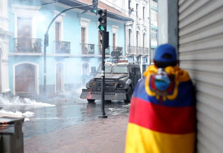 A man stands wrapped in the national flag during protests after Ecuadorian President Lenin Moreno's government ended four-decade-old fuel subsidies, in Quito