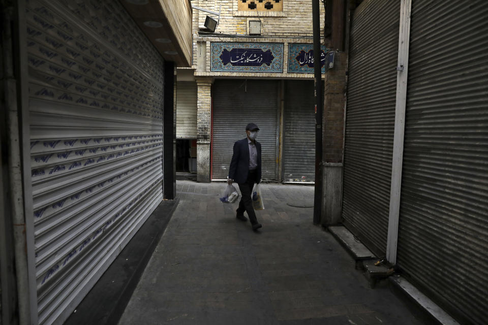 A man wearing a face mask and gloves to protect against the new coronavirus carries his shopping as he walks past closed shops at the Tajrish traditional bazaar in northern Tehran, Iran, Saturday, April 4, 2020. In the first working day after Iranian New Year holidays authorities have allowed some government offices and businesses to re-open with limited working hours, when schools, universities, and many businesses still are ordered to be closed aimed to prevent the spread of the virus. (AP Photo/Vahid Salemi)