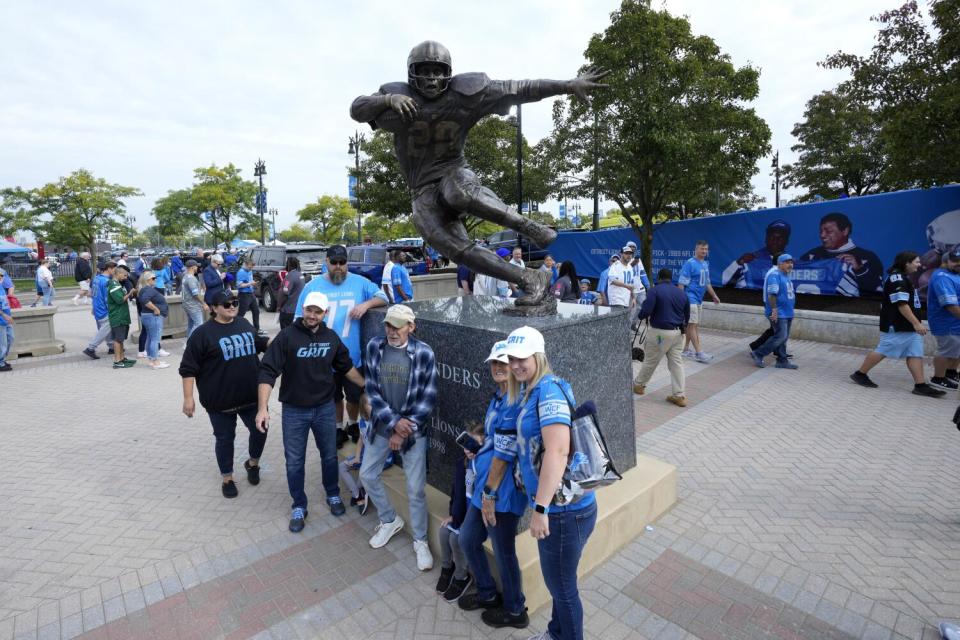 Fans pose for a photo in front of a statue of former Detroit Lions running back Barry Sanders before a 2023 game.