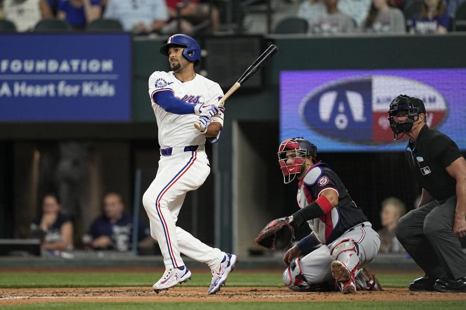 Texas Rangers' Marcus Semien follows through on a run-scoring single as Washington Nationals catcher Keibert Ruiz and umpire Jim Wolf, right, look on during the second inning of a baseball game in Arlington, Texas, Thursday, May 2, 2024. (AP Photo/Tony Gutierrez)