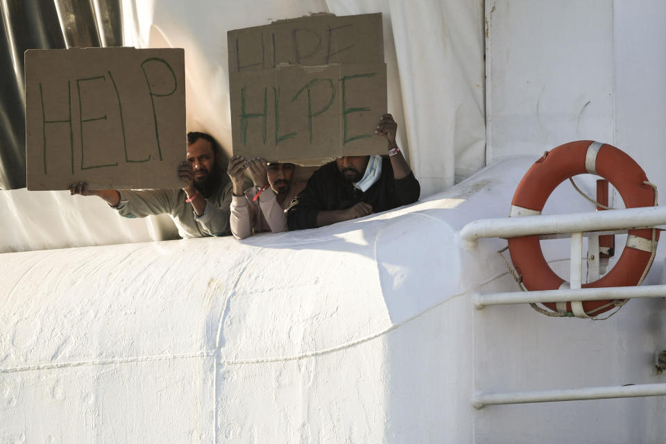 Migrants hold banners asking for help, from a deck of the Norway-flagged Geo Barents ship operated by Doctors Without Borders, in Catania's port, Sicily, southern Italy, Monday, Oct. 7, 2022. The Geo Barents has been allowed Sunday to disembark 357 migrant that Italian authorities defined as "vulnerable people" and minors, while leaving another 215 people that were declared non-vulnerable blocked on board. (AP Photo/Salvatore Cavalli)