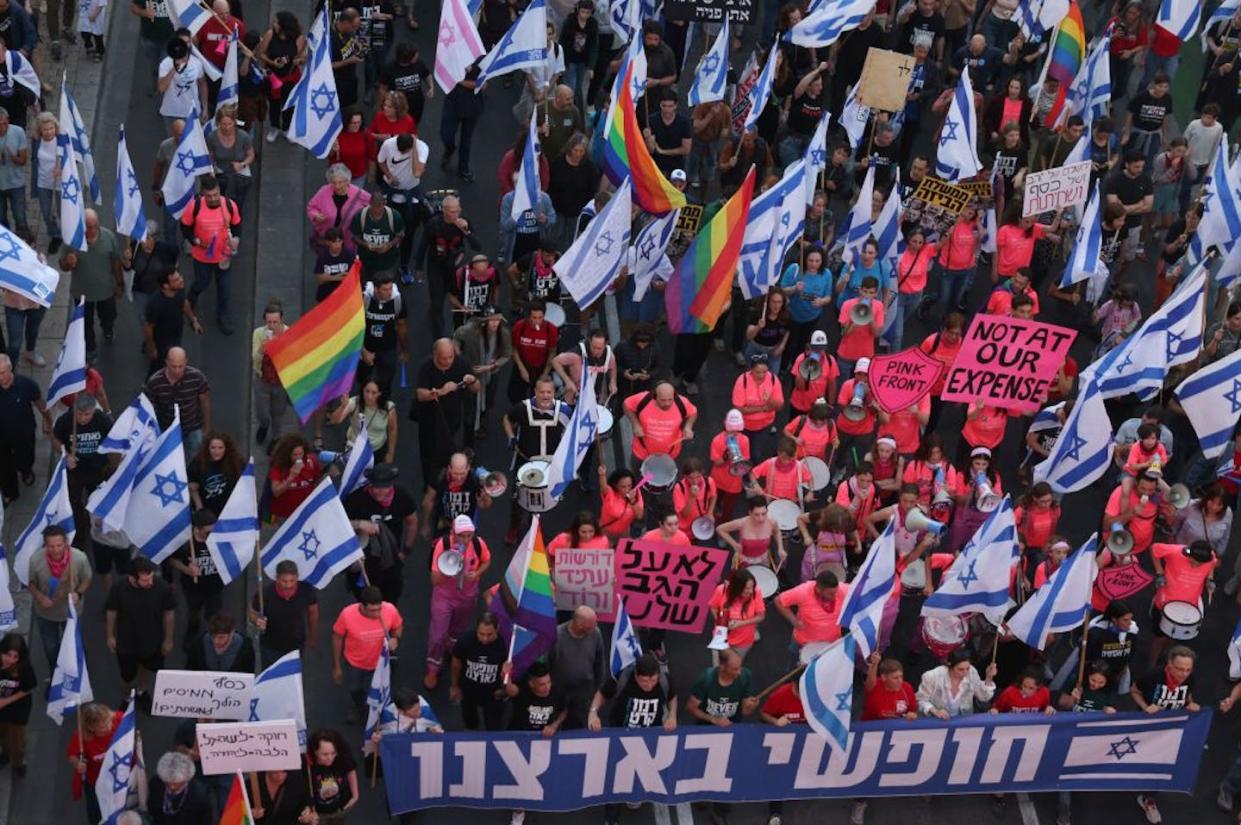 Demonstrators lift Israeli flags and LGBTQ pride flags during a protest against the proposed judicial overhaul in Tel Aviv in May 2023. <a href="https://www.gettyimages.com/detail/news-photo/demonstrators-lift-flags-and-banners-during-a-protest-news-photo/1256499783?adppopup=true" rel="nofollow noopener" target="_blank" data-ylk="slk:Ahmad Gharabli/AFP via Getty Images;elm:context_link;itc:0;sec:content-canvas" class="link ">Ahmad Gharabli/AFP via Getty Images</a>