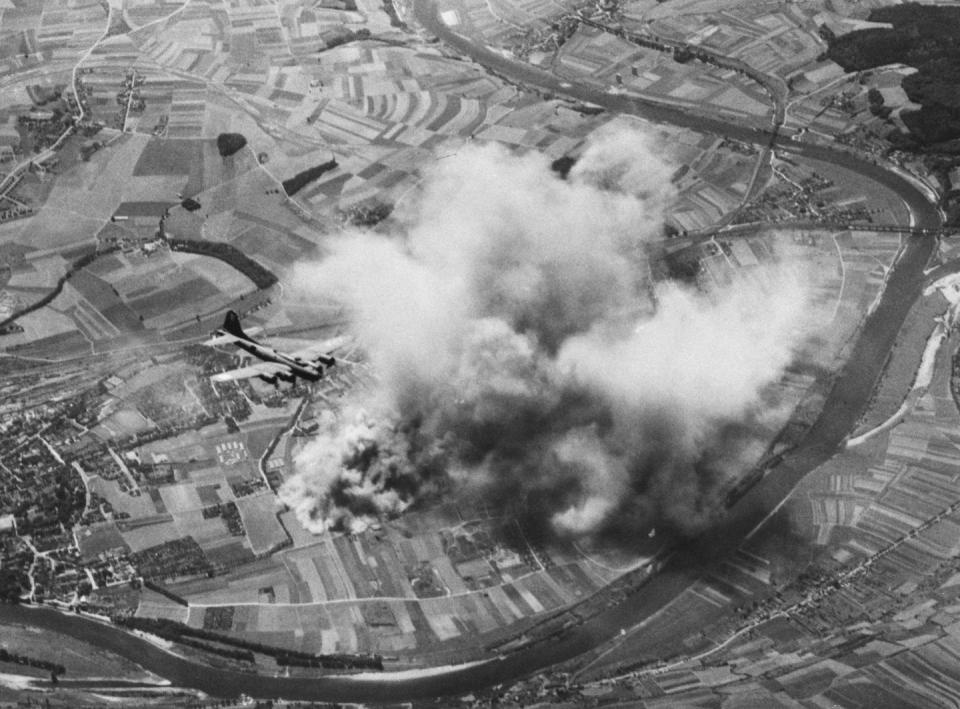 a bomber plane flying high in the sky over a factory engulfed in smoke