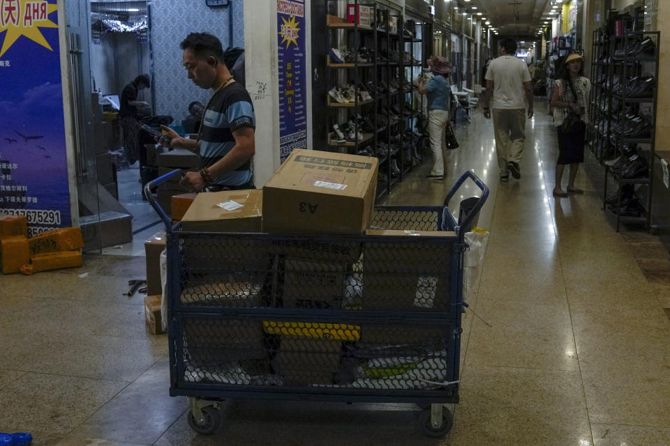 A delivery worker pushes a cart loaded with goods as women shop for shoes at Ritan International Trade Center in Beijing on Wednesday, May 15, 2024. Data released on Friday, May 17 showed housing prices in China slumped for the first four months of the year, although factory output rose nearly 7%, as the country prepares to announce fresh measures to reinvigorate its ailing property industry. (AP Photo/Andy Wong)
