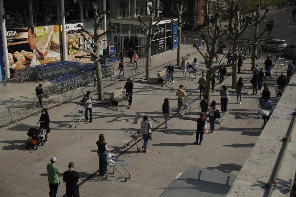 People observe social distancing in an attempt to stop the spread of coronavirus by standing behind tape lines as they queue up to shop outside a branch of the Tesco supermarket chain in west London, Friday, April 10, 2020. (AP Photo/Matt Dunham)