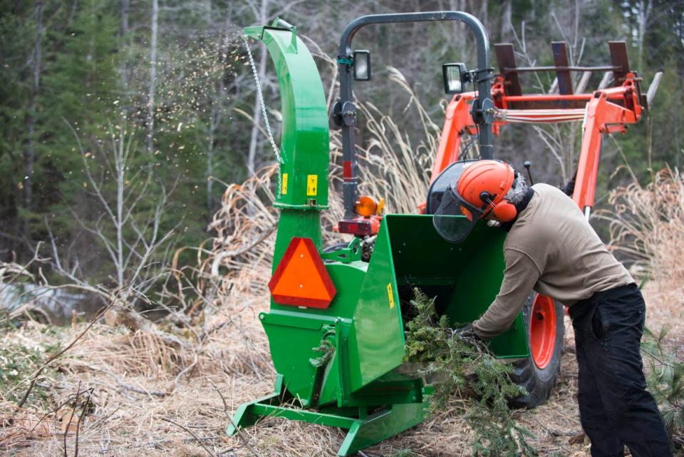 A person in a red helmet feeds a tree into a wood chipper in the woods.