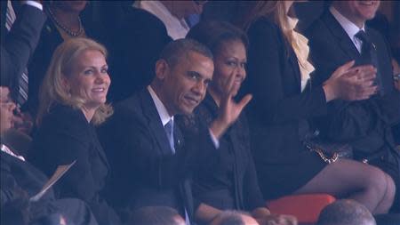 U.S. President Barack Obama (C) waves to the crowd alongside his wife, first lady Michelle Obama (R) and Denmark's Prime Minister Helle Thorning-Schmidt in this still image taken from video courtesy of the South Africa Broadcasting Corporation (SABC) at the First National Bank (FNB) Stadium, also known as Soccer City, during former South African President Nelson Mandela's national memorial service in Johannesburg December 10, 2013. REUTERS/SABC via Reuters TV