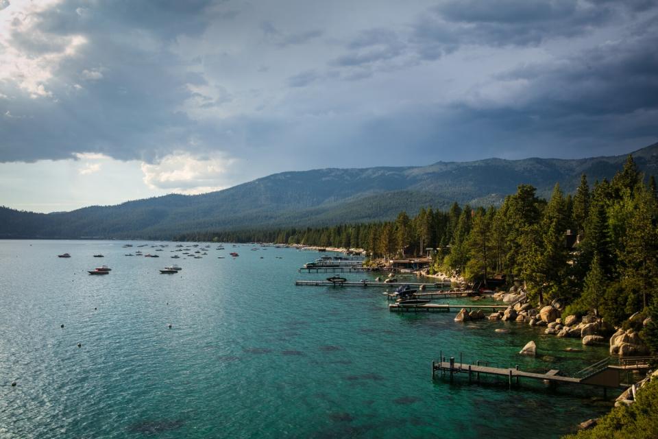 The Lake Tahoe shoreline with boats in the water and trees and big rocks along the shore.