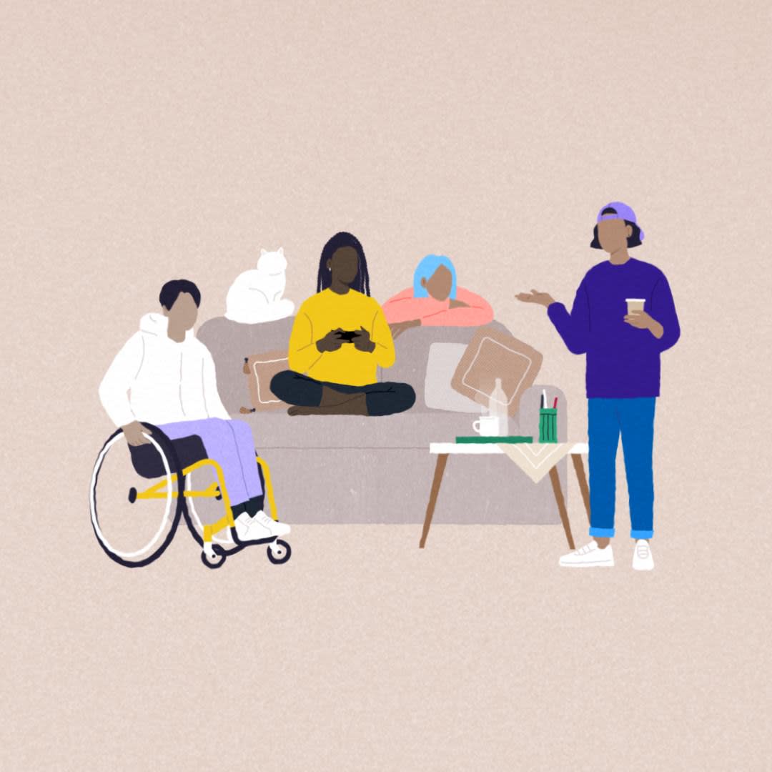 4 friends mingling by a couch, one is sitting in a wheelchair, one is curled up on the couch, one is behind it, one is standing with a cup of coffee