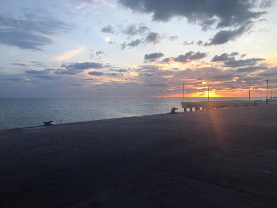 A view of the sun setting over the horizon seen from an empty stretch of beach.