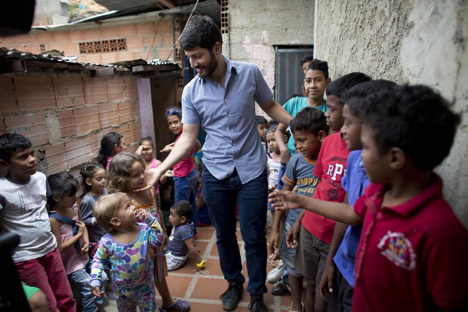 In this Aug. 26, 2018 photo, Roberto Patino greets children at a children's center in the La Vega neighborhood of Caracas, Venezuela. Patino, a rising star in Venezuela's unravelling opposition movement, and other grassroots organizers in their 20s and 30s have been feeding children, encouraging women to become community activists and organizing protests to demand public services like reliable drinking water and electricity. (AP Photo/Ariana Cubillos)