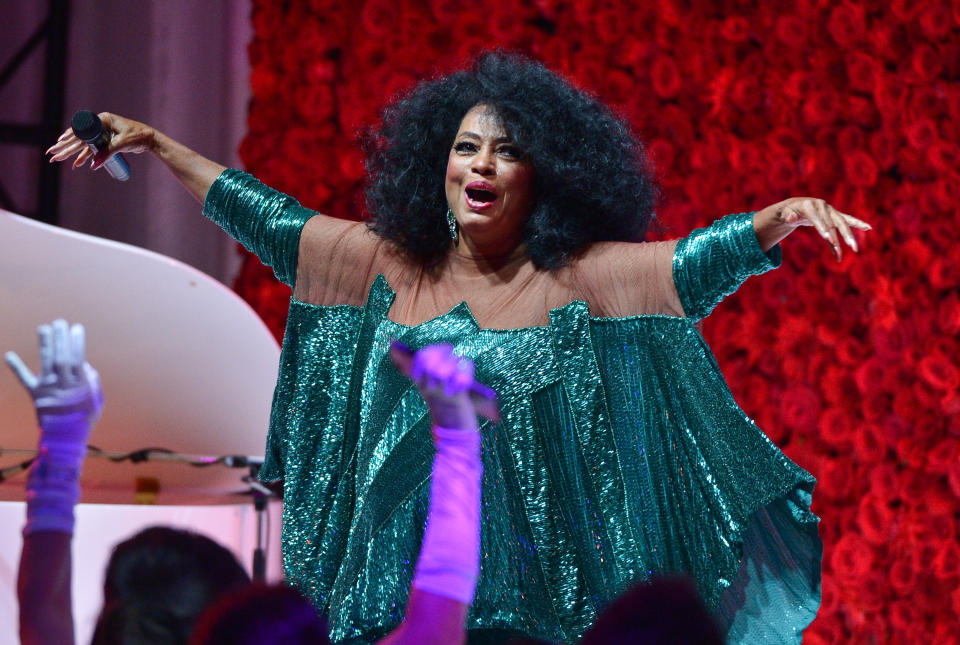 Performer in a sparkling green dress with flared sleeves, singing on stage