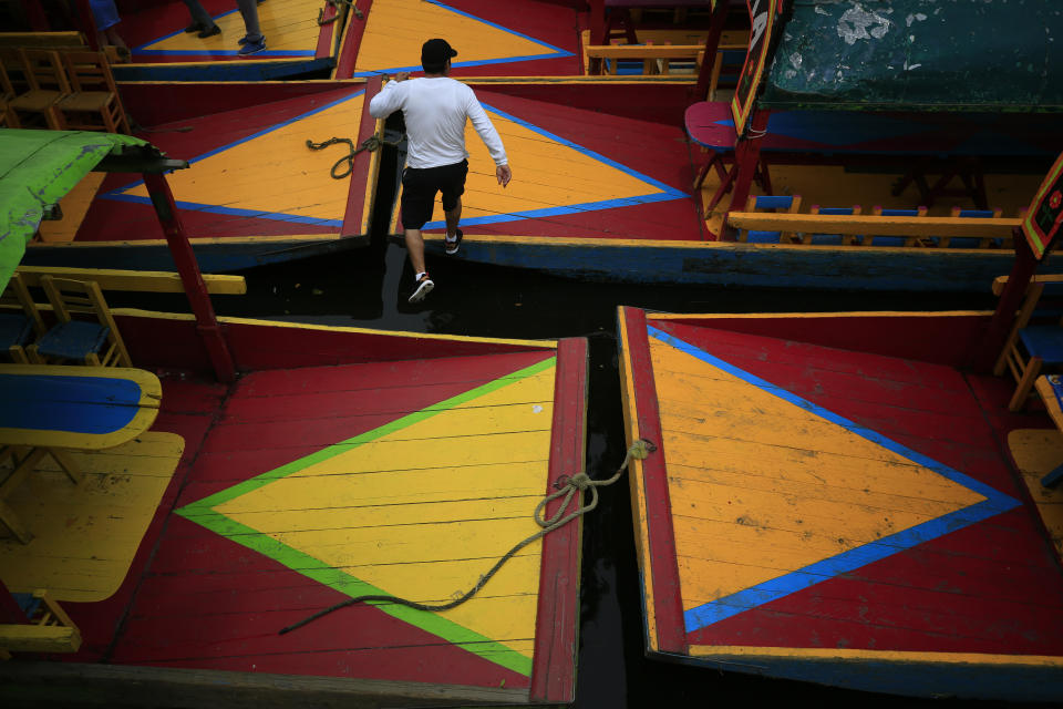A worker leaps between parked trajineras, the colorful boats typically rented by tourists, families, and groups of young people, in Xochimilco, Mexico City, Friday, Sept. 6, 2019. The usually festive Nativitas pier was subdued and largely empty Friday afternoon, with some boat operators and vendors estimating that business was down by 80% on the first weekend following the drowning death of a youth that was captured on cellphone video and seen widely in Mexico. Borough officials stood on the pier to inform visitors of new regulations that went into effect Friday limiting the consumption of alcohol, prohibiting the use of speakers and instructing visitors to remain seated.(AP Photo/Rebecca Blackwell)
