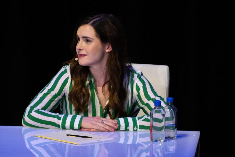 A woman in a green striped shirt sitting at a debate table