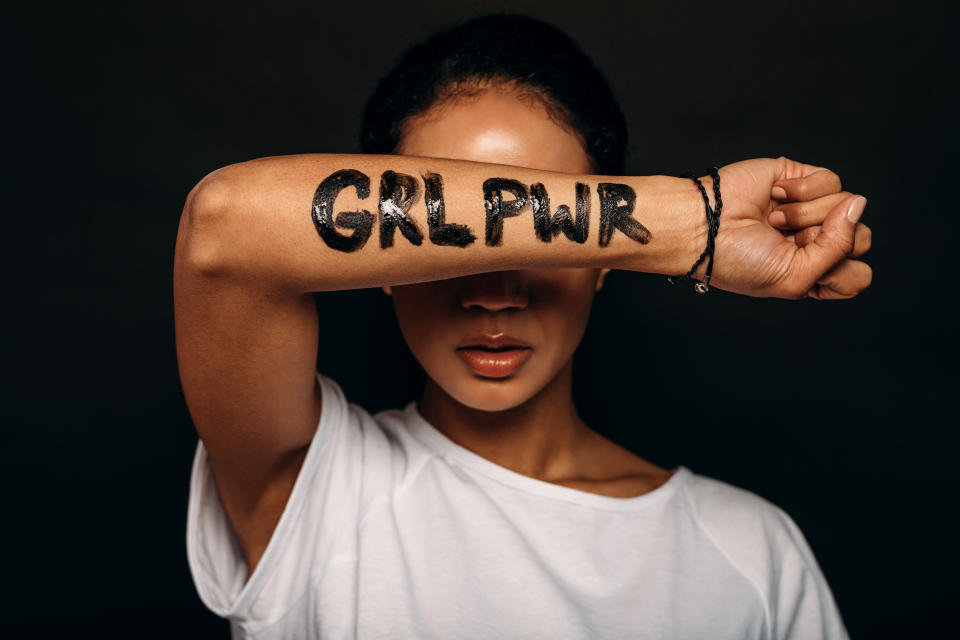 Woman with letters "GRL PWR" written on her hand. Portrait of a woman with arm covering a part of her face.